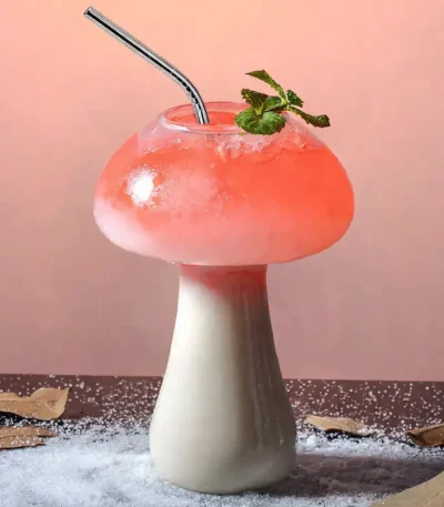 Copo em forma de cogumelo contendo um cocktail rosa com um ramo de hortelã, decorativo e original.