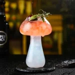 Copo de cocktail com bebida colorida e guarnição de hortelã e cereja.