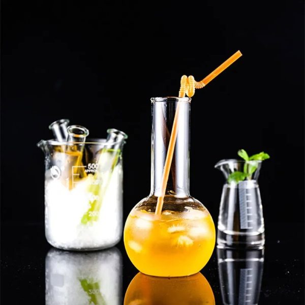Vaso de laboratório contendo uma bebida laranja com um canudo, acompanhado de outros acessórios de laboratório em vidro, sobre fundo preto.