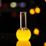Vaso de laboratório em vidro contendo um líquido amarelo vivo, usado para experiências científicas ou como decoração de inspiração científica.