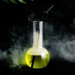 Vaso de laboratório contendo um líquido fluorescente amarelo com um tubo de vidro e fumaça ao redor, evocando uma experiência científica misteriosa.