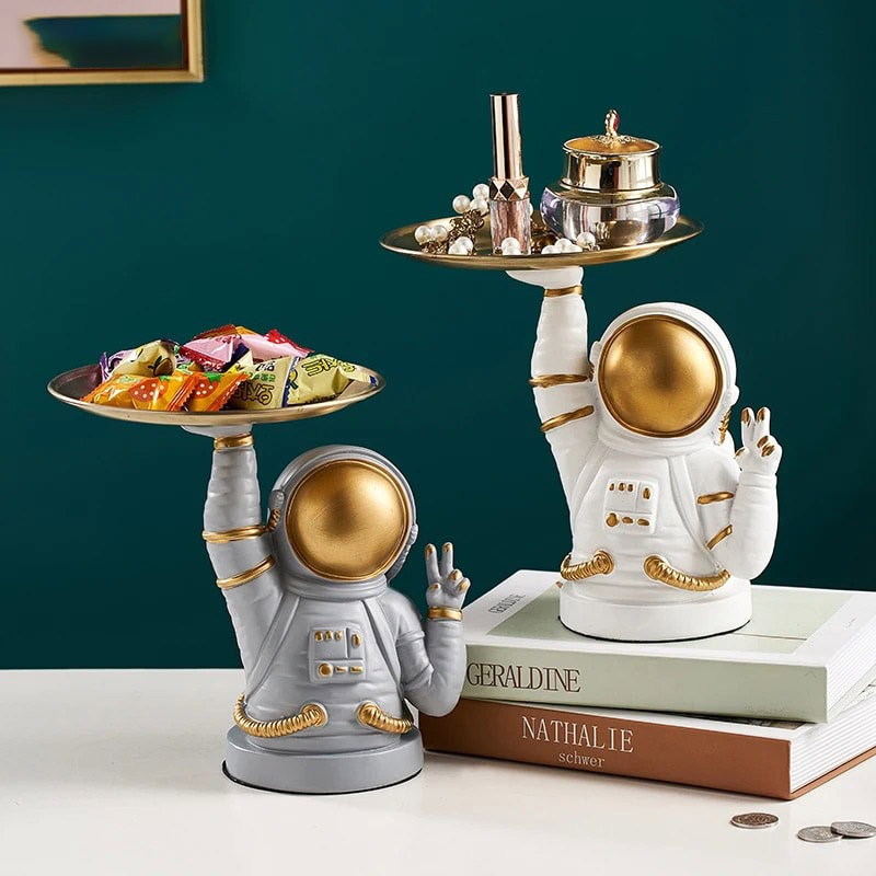 copos-astronautas-peace-1 Figura de astronauta em cerâmica branca e dourada, usada como decoração, segurando uma bandeja com objetos de decoração e doces, estilo moderno e original.