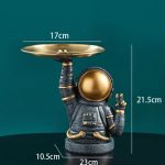Vaso decorativo em forma de astronauta com uma bandeja dourada, ideal para decoração científica ou moderna.