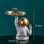 Porta-utensílios original em forma de astronauta com uma bandeja dourada, perfeito para decoração de cozinha ou como objeto de coleção científica. Design único e divertido para os amantes do espaço.
