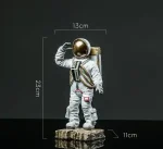 Figura de astronauta em miniatura com capacete dourado, medindo 23,5 cm de altura, 13 cm de largura e 11 cm de profundidade, ideal para decoração científica ou de coleção.