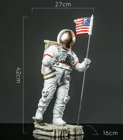 Figura de astronauta com bandeira americana, altura de 42 cm, dimensões 27x16 cm, representando um explorador espacial em traje completo, em pé sobre uma base rochosa.