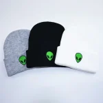 Três bonés de tecido cinza, preto e branco com um logotipo de extraterrestre verde, perfeitos para um estilo casual ou geek.