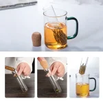 Caneca de chá em vidro com infusor, contendo chá infundido, sobre fundo branco.