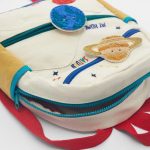 Mochila escolar branca com decoração científica, apresentando patches de pelúcia de átomos e elementos químicos, ideal para crianças apaixonadas por ciências.