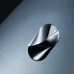 Escultura contemporânea em metal com formas fluidas e superfícies refletoras, exposta em um espaço minimalista.