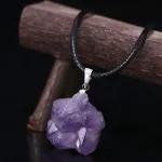 Pingente em cristal de ametista bruto suspenso num cordão preto, ideal para decoração ou uso pessoal.
