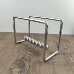 Pêndulo de Newton em metal com esferas suspensas, ideal para decoração de escritório ou espaço científico.