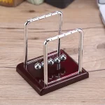 Pêndulo de Newton em metal e madeira, ferramenta científica para demonstração das leis da física, perfeito para ensino e decoração de estilo científico.