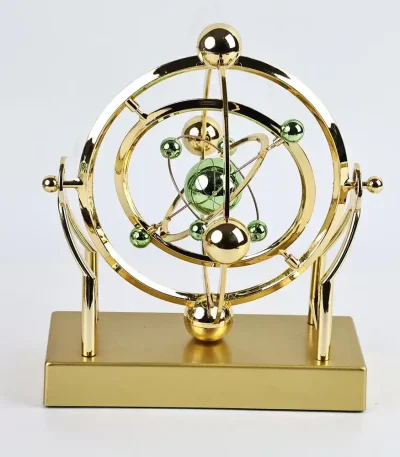 Modelo atômico decorativo em metal dourado com esferas verdes e douradas, representando um átomo estilizado.