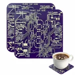 Placa de circuito impresso roxa com inscrições "PLACE CUP HERE" e uma xícara de café colocada sobre um circuito impresso.