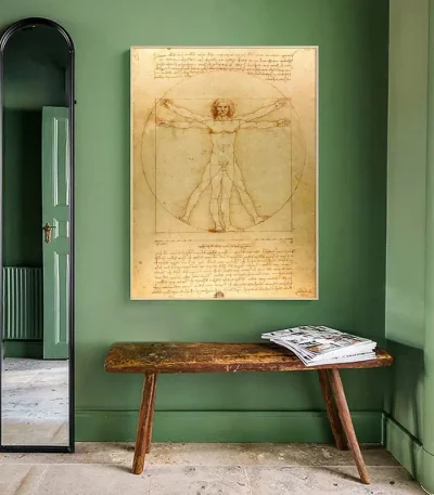 Reprodução do famoso desenho de Leonardo da Vinci, representando o homem de Vitrúvio com suas proporções ideais, exibido em uma parede verde em uma sala elegante.