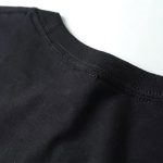 Close-up de uma t-shirt preta em algodão com costura visível na gola, destacando a textura suave e o acabamento cuidadoso da peça.