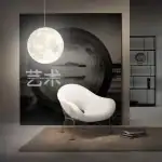 Lampe murale en forme de lune suspendue au-dessus d'un fauteuil moderne blanc dans un intérieur contemporain, avec étagère en arrière-plan.