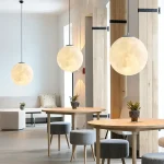 Suspensão luminosa em forma de lua, decoração interior moderna com três lâmpadas suspensas redondas, ambiente acolhedor e design limpo em um espaço contemporâneo.