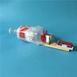 Robô educativo feito a partir de uma garrafa de plástico reciclada, com um motor, uma roda em forma de coelho vermelho e uma plataforma de madeira, ilustrando criatividade e reciclagem.
