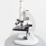 Microscópio científico branco para observação precisa em laboratório ou em casa. Ideal para o estudo de pequenos objetos, células ou micro-organismos com alta resolução.