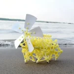 Veículo científico em miniatura em plástico amarelo com hélice branca, posicionado na areia perto do mar, ilustrando um objeto de decoração científica original e educativo.