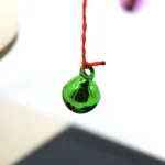 Bola de vidro verde suspensa por um fio vermelho, objeto científico decorativo, destacando a transparência e a cor vibrante do vidro.