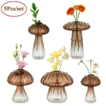 Vasos de vidro transparente com tampa em forma de cogumelo, contendo flores artificiais coloridas, ideal para decoração de casa ou escritório.