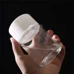 Copo de cocktail transparente com tampa de silicone branco, segurado por uma mão, sobre fundo preto.