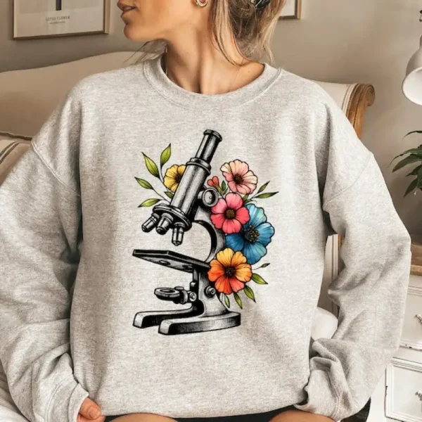 Microscópio ilustrado com flores coloridas em um sweatshirt cinza, combinando ciência e natureza em um estilo moderno e na moda.