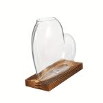 Vaso de vidro transparente em forma de coração, colocado sobre uma base de madeira natural, ideal para a decoração científica ou artística.